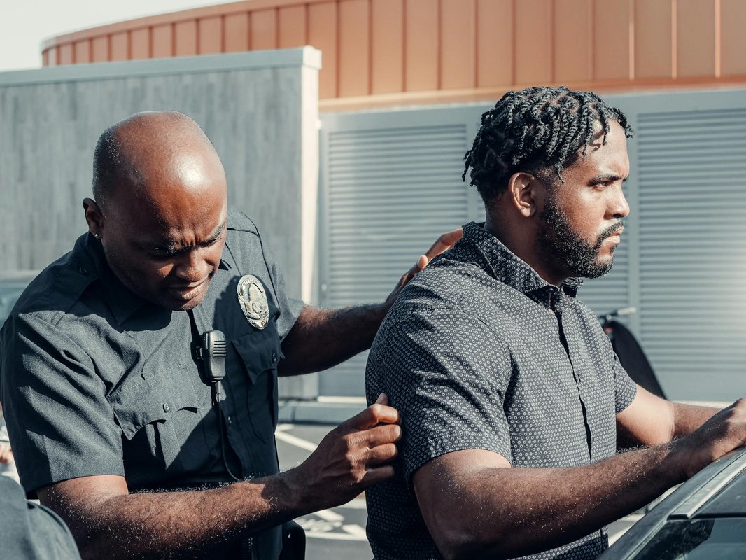 A police officer handcuffs a suspect in a dramatic arrest scene outdoors in daylight.