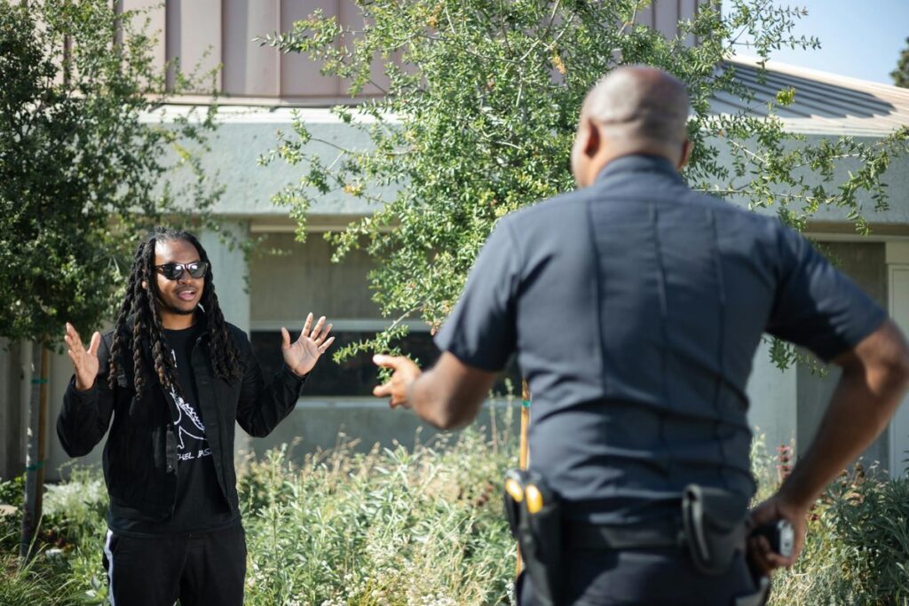 A police officer engages with a civilian raising hands outdoors, signifying communication or questioning.