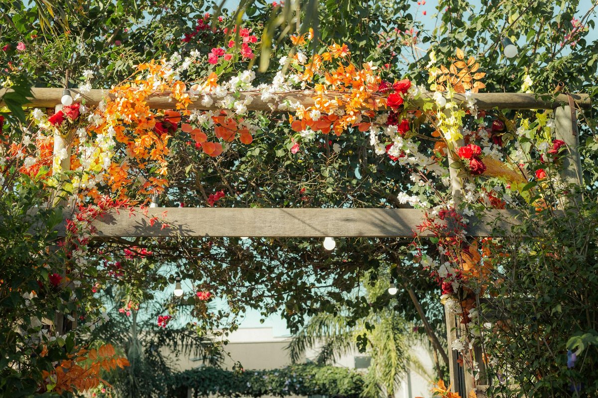 A colorful floral wedding arch adorned with vibrant flowers under a sunny sky.