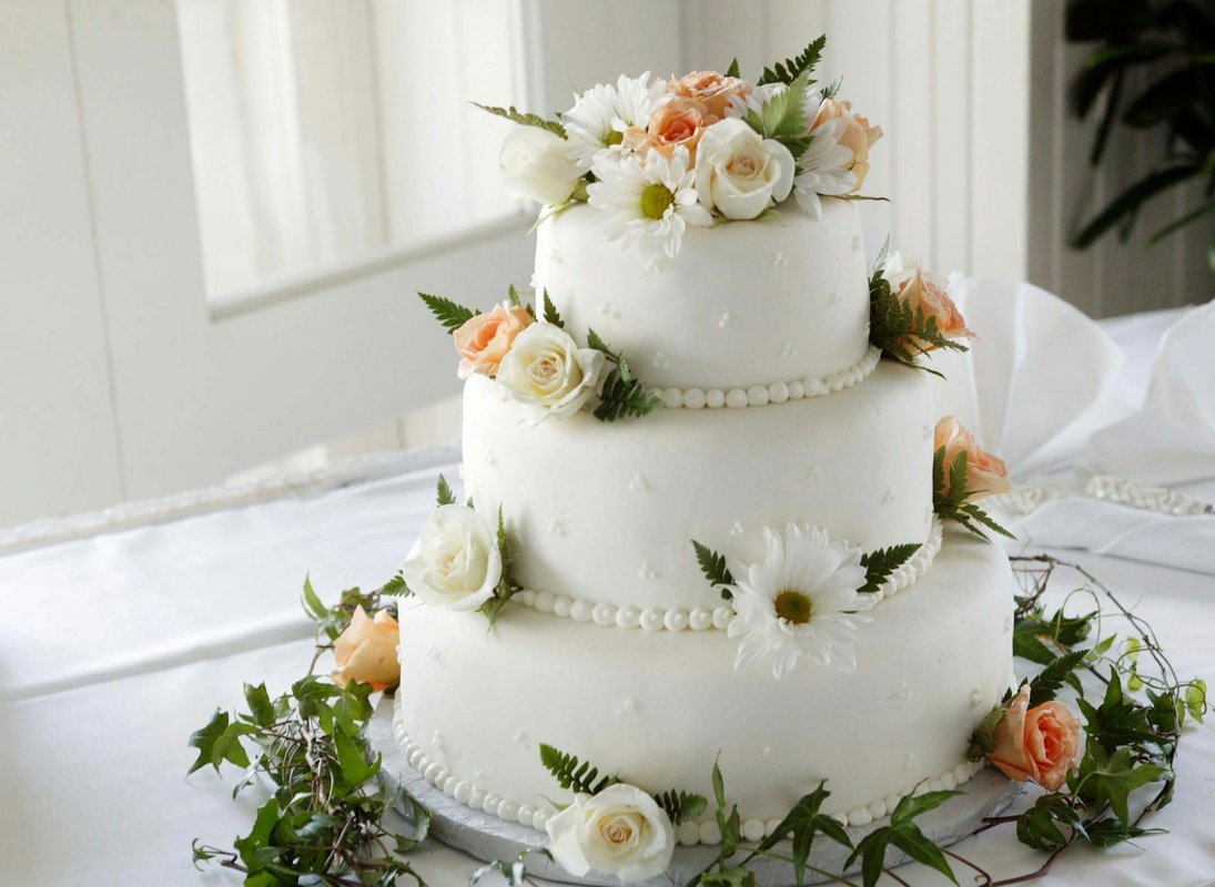 Elegant white wedding cake adorned with fresh roses and daisies, perfect for a romantic celebration.