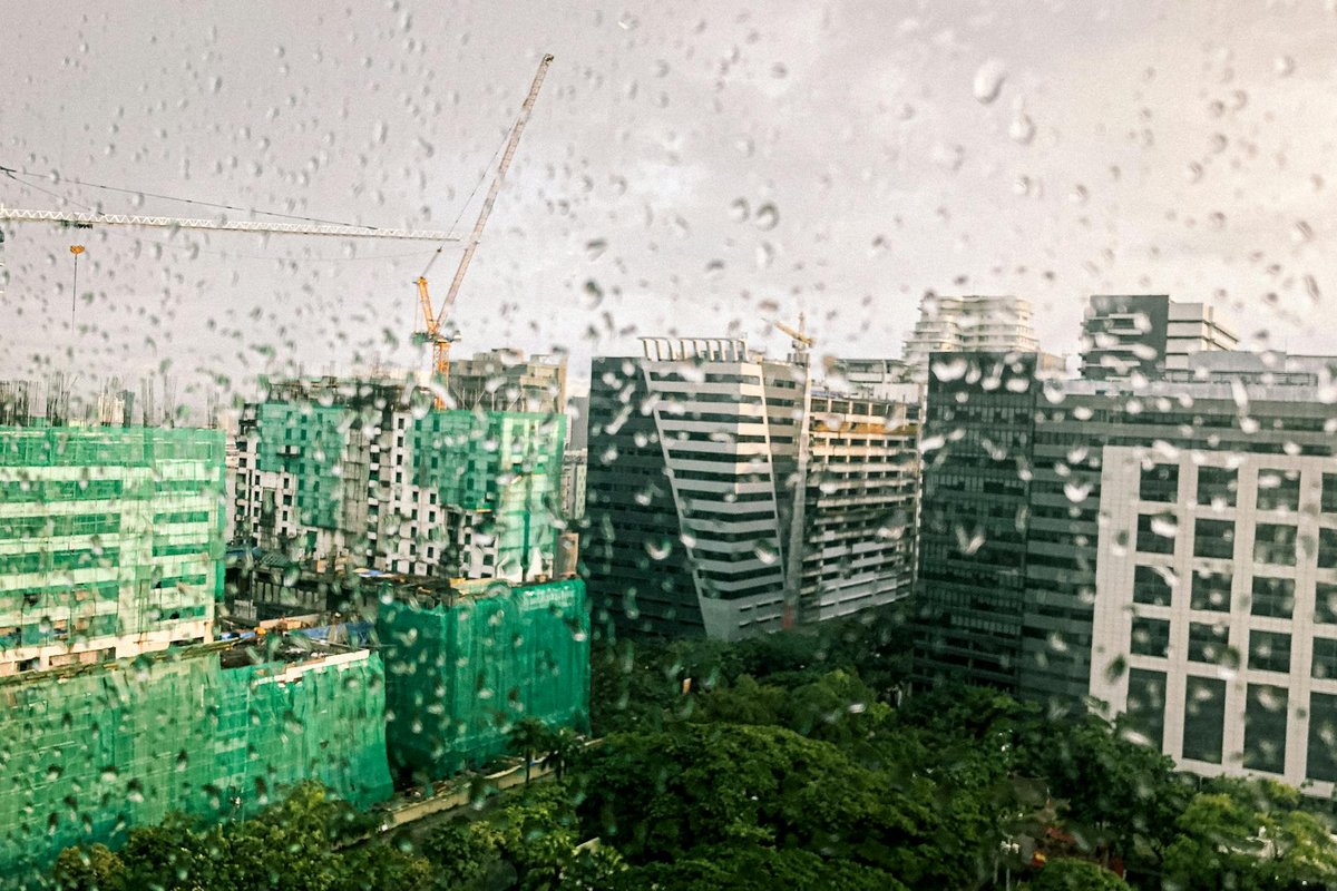 View of modern city buildings seen through a rain-covered window, creating a moody atmosphere.