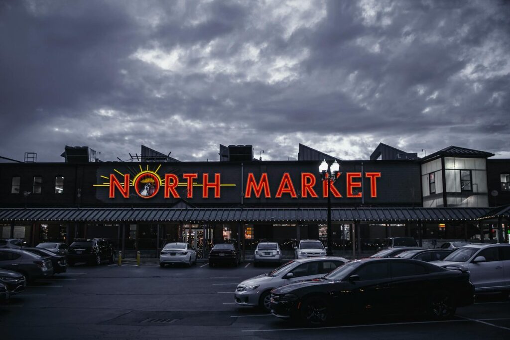 View of North Market in Columbus, Ohio with neon lights and parked cars under a cloudy night sky.