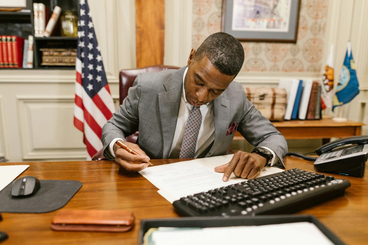 Professional man signs contract at desk in classic office environment.