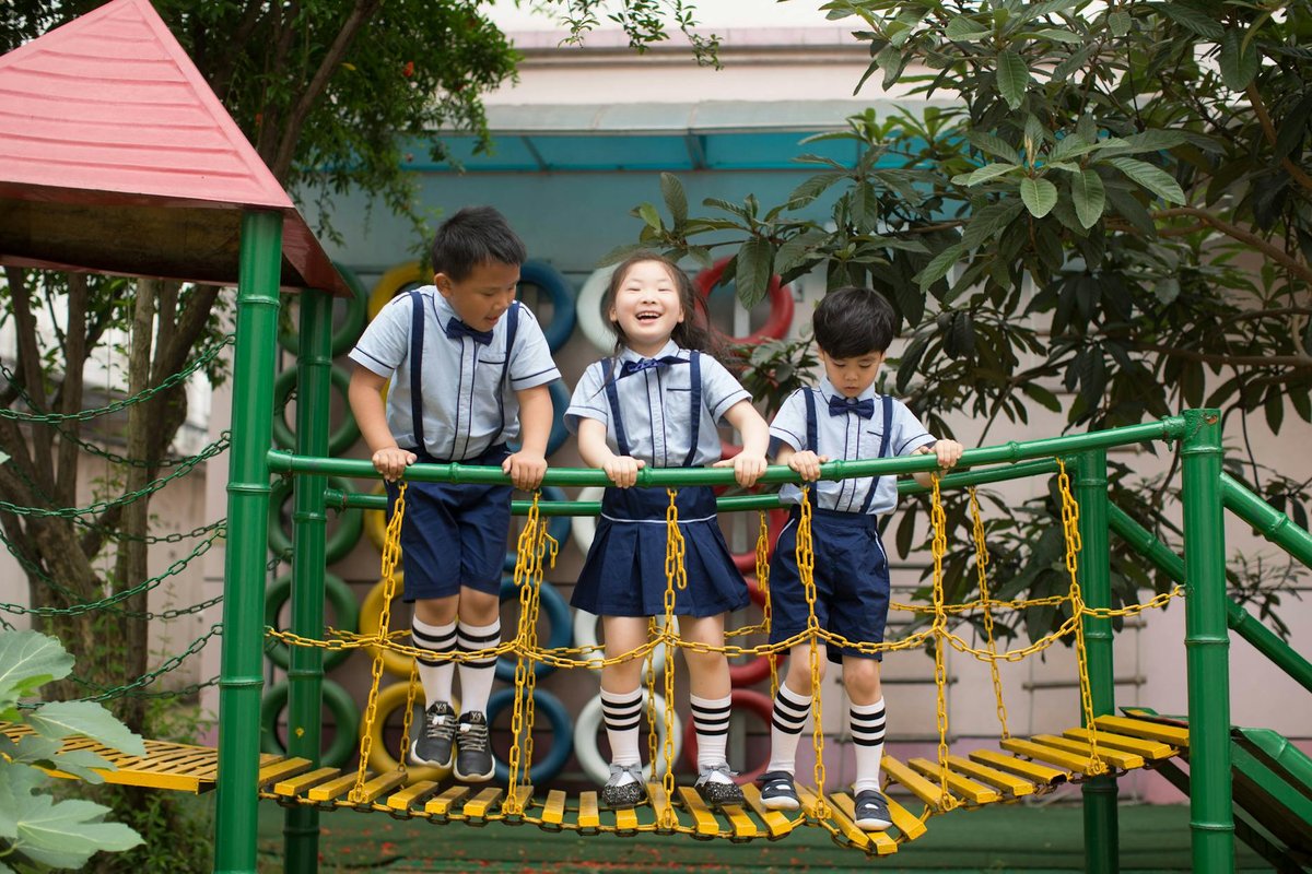 Three children in school uniforms enjoy playing on a vibrant playground bridge.