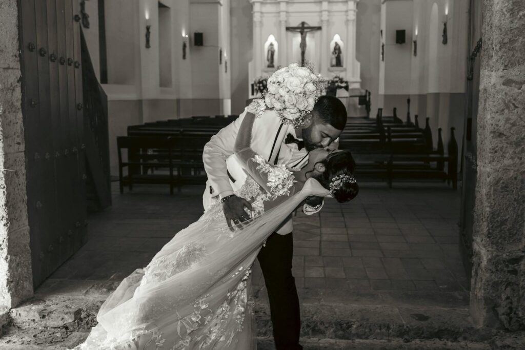Bride and groom share a romantic kiss at their church wedding. Timeless love captured in black and white.