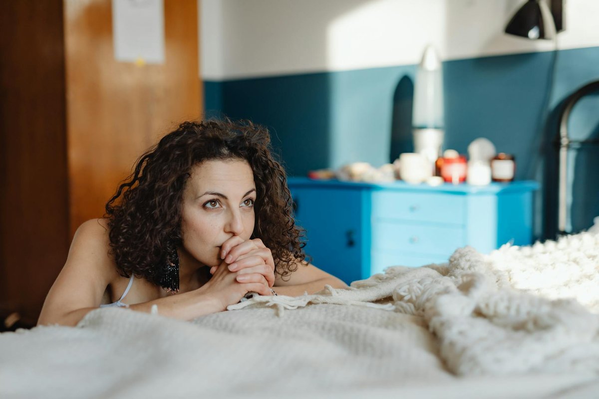 Thoughtful woman lying on bed in cozy room with blue accents, enjoying a peaceful moment.