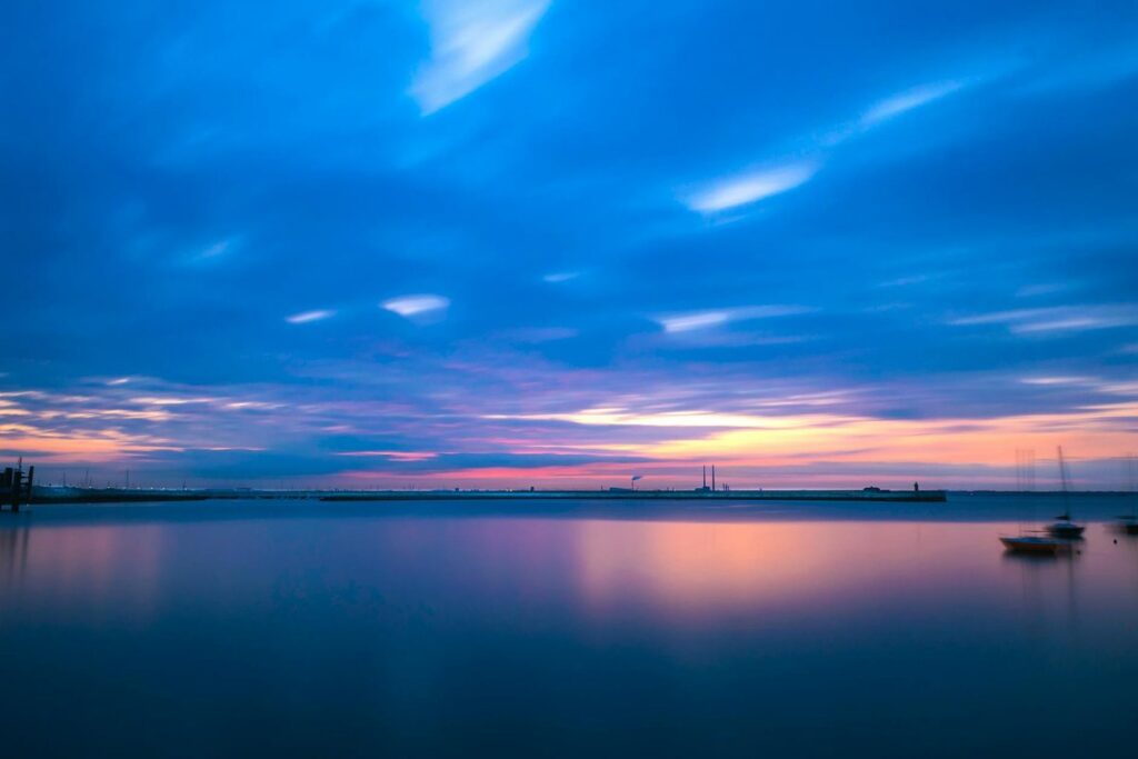 A serene sunset over Dublin Bay with calm waters and boats, creating a peaceful ambiance.
