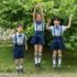 Three children in school uniforms jumping happily outdoors in a lush park setting.