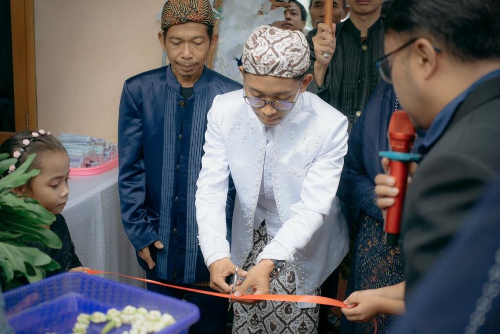 Man in traditional attire cuts ribbon at an indoor event celebration.