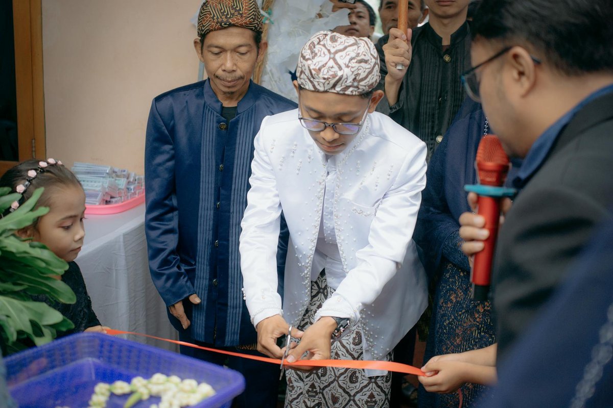 Man in traditional attire cuts ribbon at an indoor event celebration.