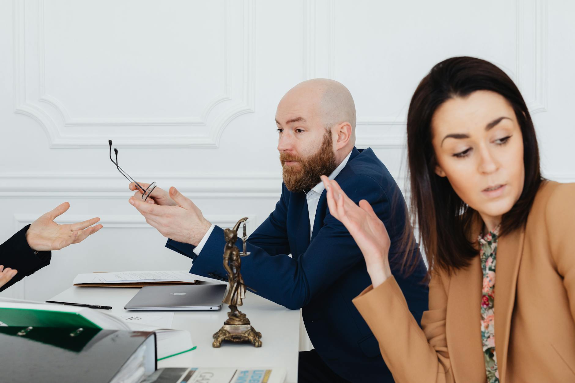 A businessman working on a laptop in an office with a Lady Justice statue in focus on the desk.