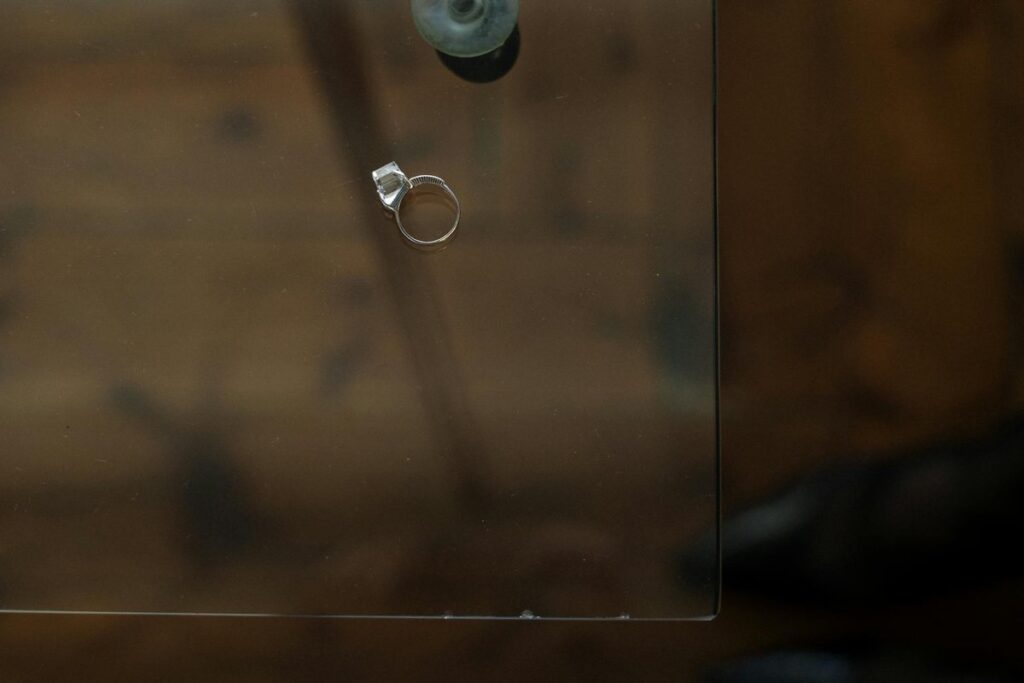 A single engagement ring rests on a glass table, symbolizing relationship reflection.