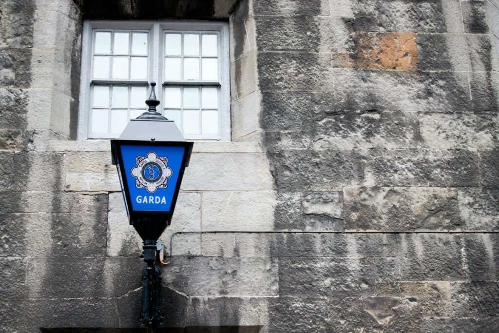 A classic Garda street lamp mounted on a weathered stone wall in Dublin, Ireland.