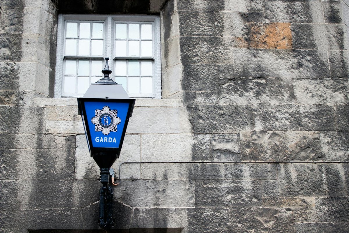 A classic Garda street lamp mounted on a weathered stone wall in Dublin, Ireland.