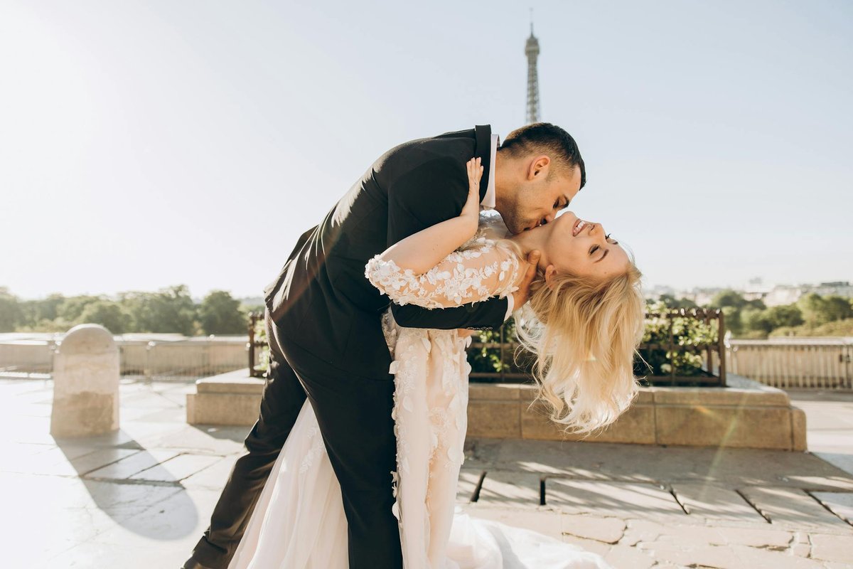 A joyful bride and groom kiss with the Eiffel Tower in the background, symbolizing love and togetherness in Paris.