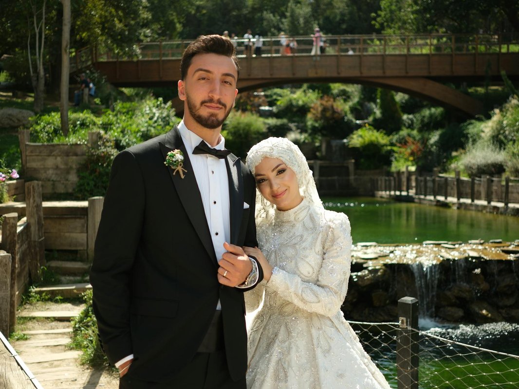 Bride and groom pose elegantly in nature beside a serene pond and wooden bridge.
