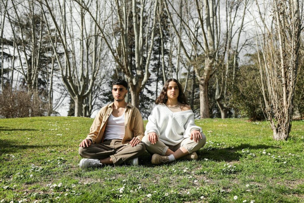 A peaceful couple practicing meditation in a tranquil park surrounded by nature.