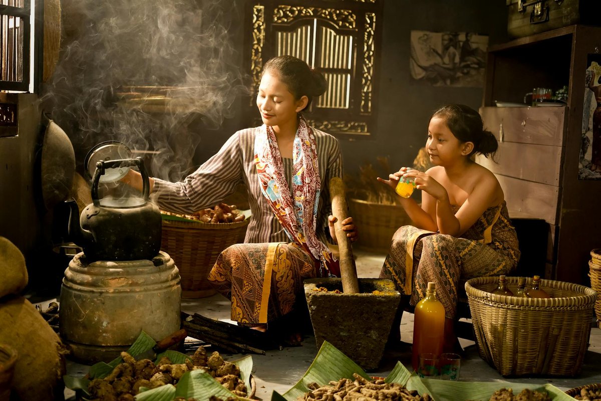 Indonesian mother and child in a traditional kitchen setting preparing herbs and drinks.