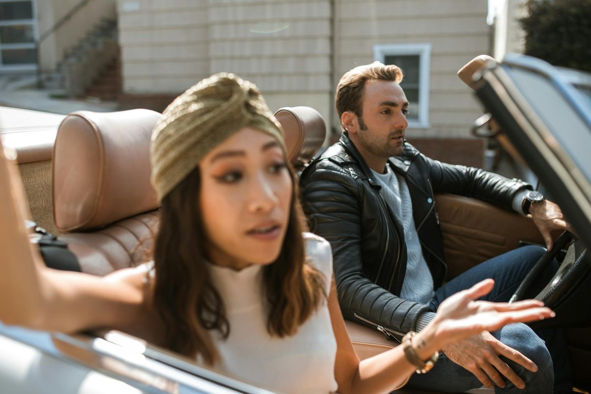 A couple having an animated discussion inside a convertible car on a sunny day.
