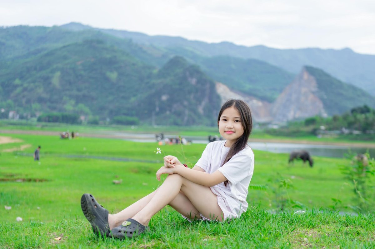 A young girl relaxing on a grassy field in a mountainous area, enjoying a peaceful outdoor setting.
