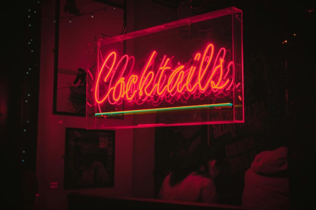 Bright neon 'Cocktails' sign glowing in a lively Dublin bar at night.