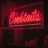 Bright neon 'Cocktails' sign glowing in a lively Dublin bar at night.