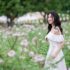 Asian woman in a white dress elegantly standing in a vibrant meadow with flowers.