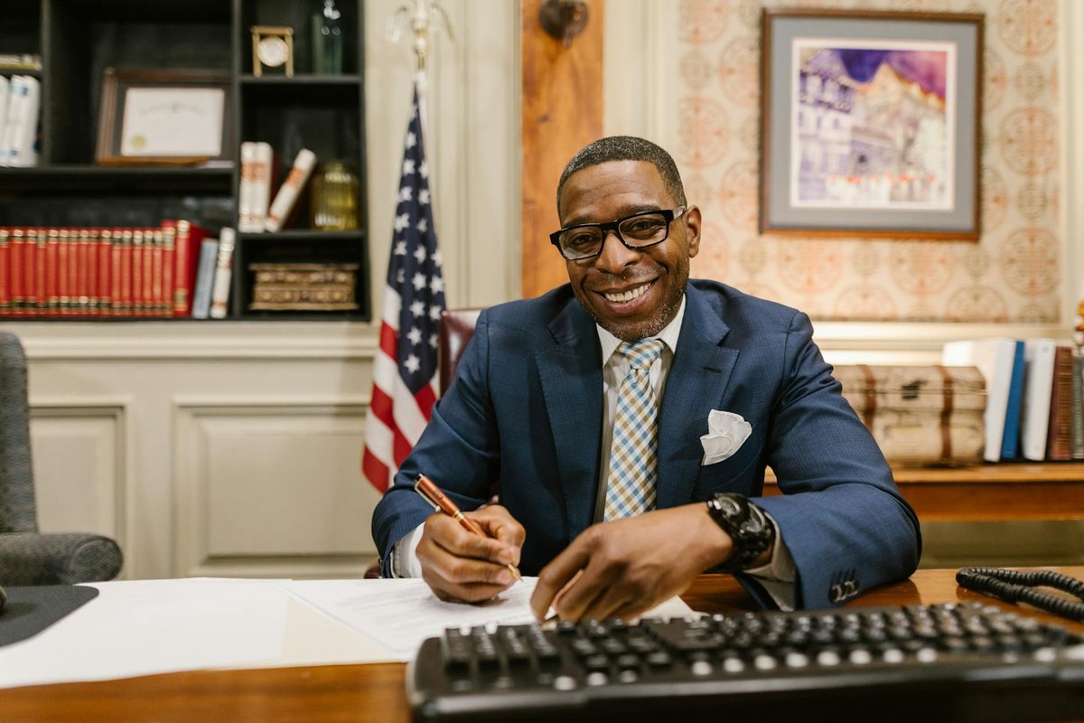 Smiling lawyer writing documents in a well-decorated office setting with legal books and US flag.