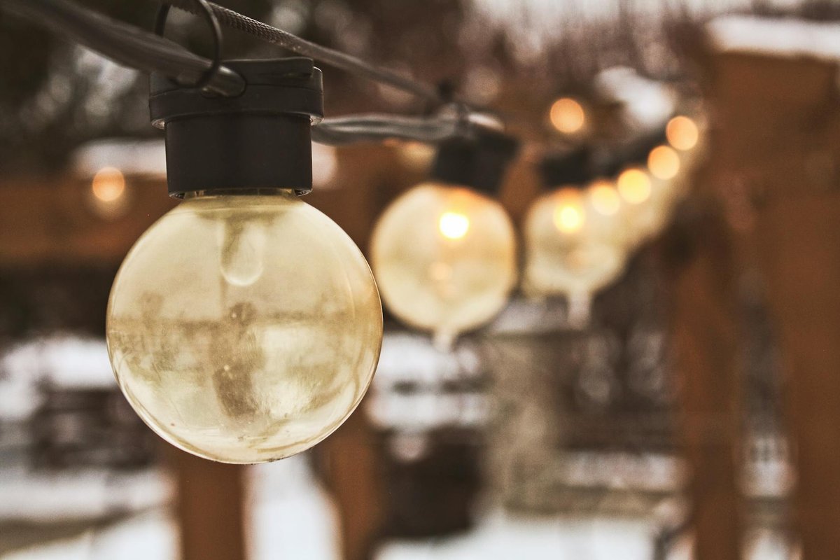 Cozy close-up of string lights glowing warmly in a snowy outdoor background.