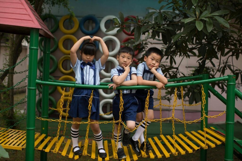 Three children in uniform having fun on a vibrant playground bridge outdoors.