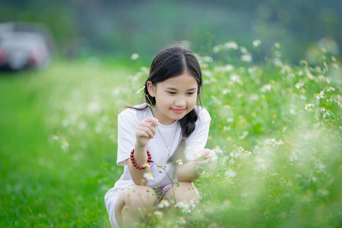 A young girl smiling in a lush green meadow with blooming flowers in Hà Nội, Vietnam.