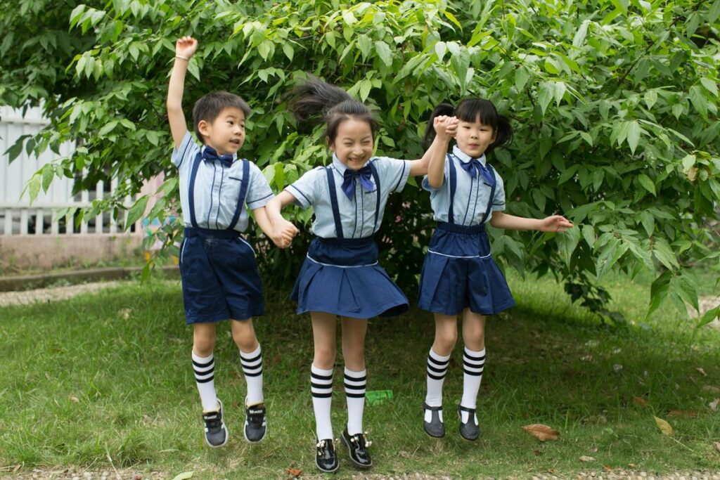 Three cheerful children in blue school uniforms jumping happily outdoors.
