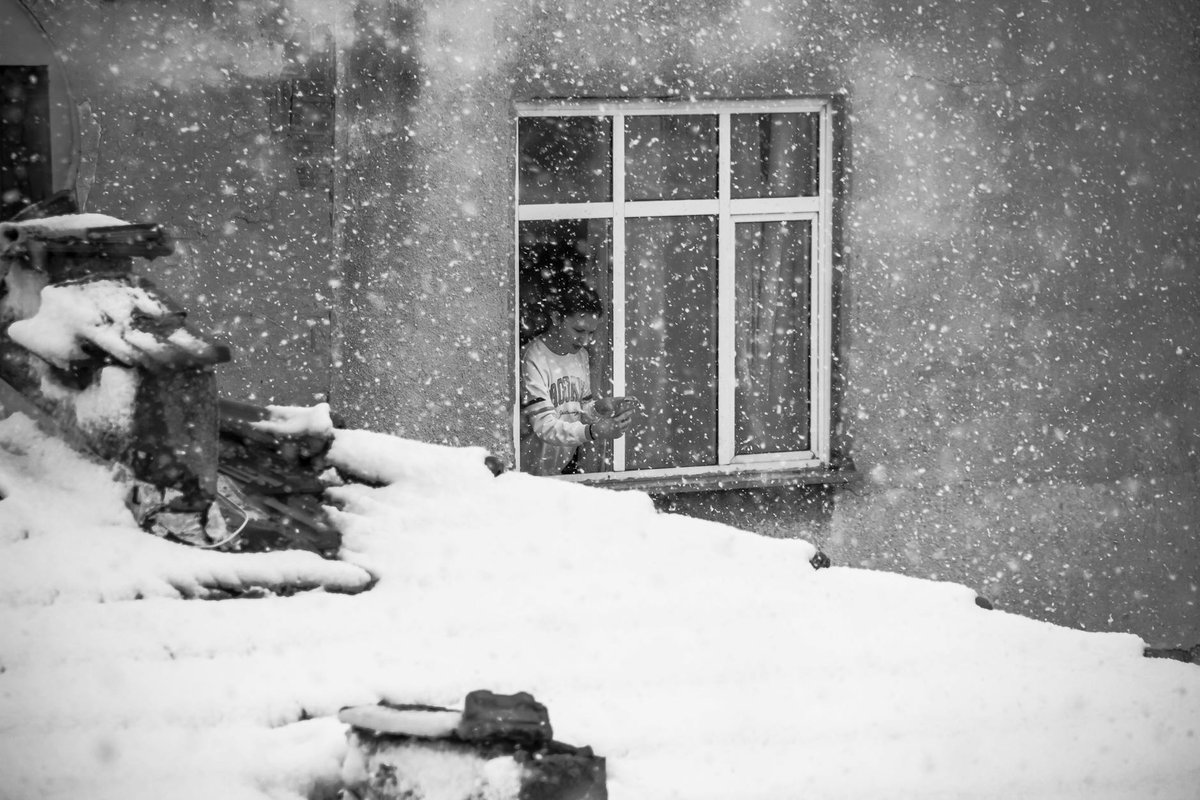 A child gazes out a window as snowflakes fall on a winter day.