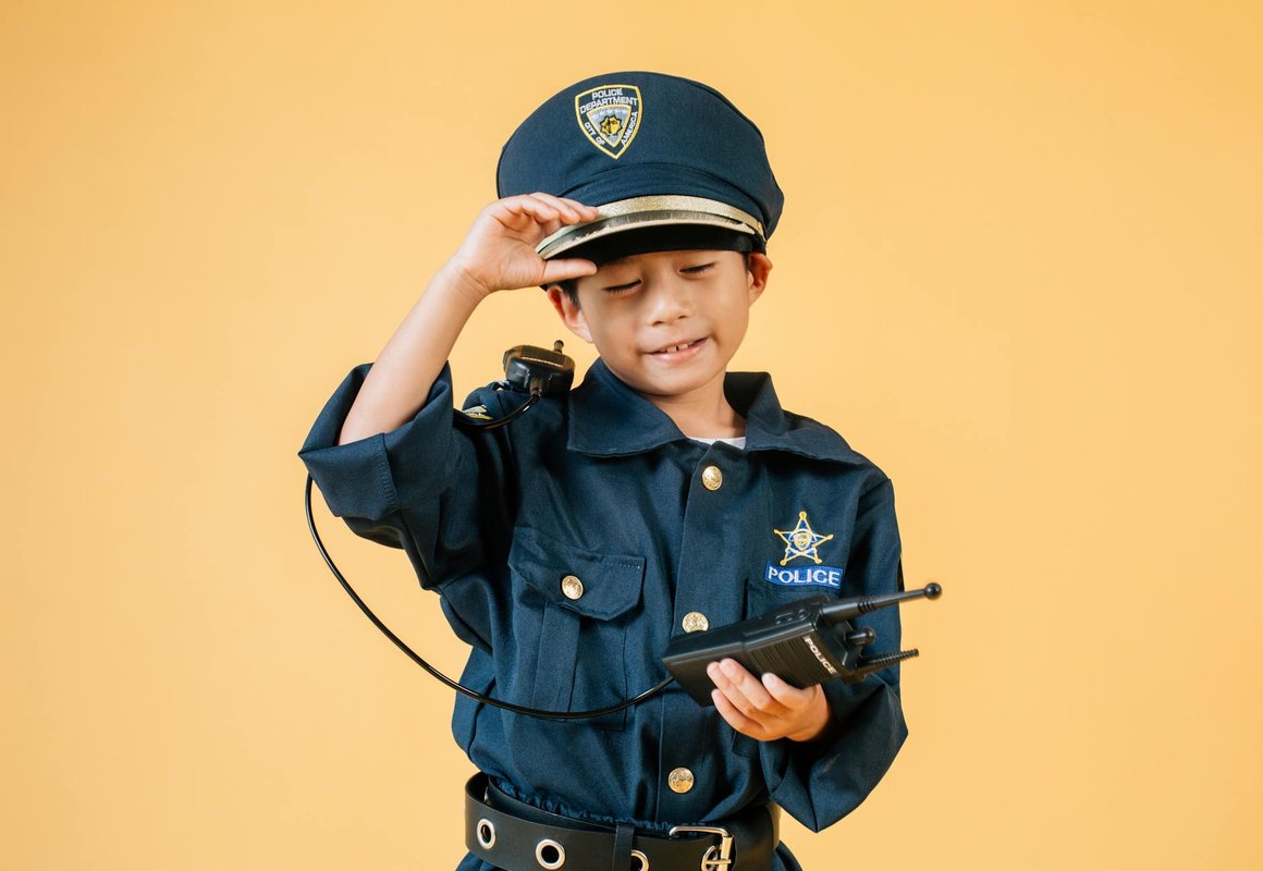 Young boy in police uniform smiling with a walkie-talkie against yellow background.