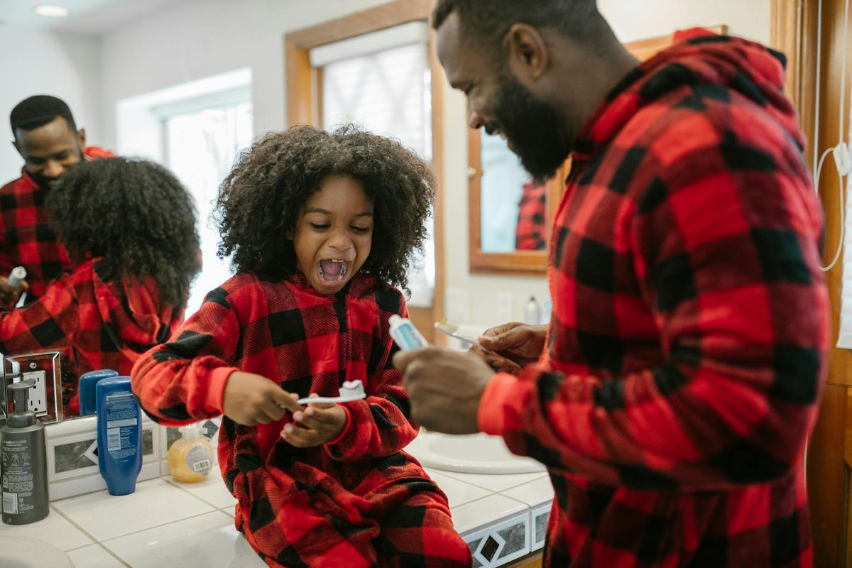 A happy father and daughter in matching pajamas brushing teeth in a bright bathroom.
