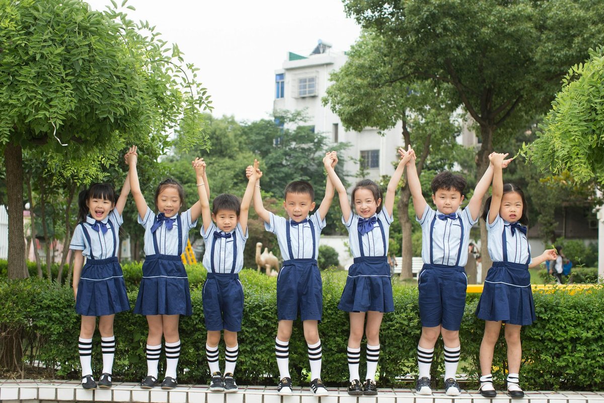 A group of smiling children in uniform holding hands outside, showcasing unity and friendship.