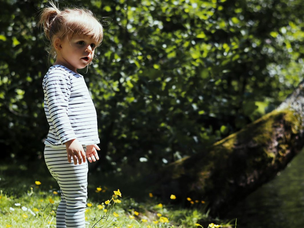A little girl in striped outfit exploring a sunlit park, surrounded by nature.