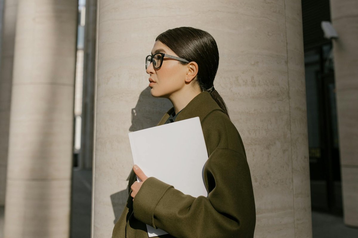Side view of a professional woman holding documents outdoors, showcasing a modern business look.