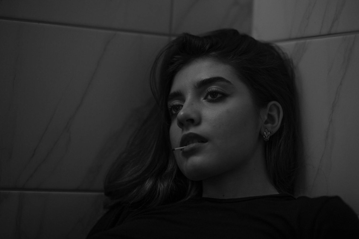 Black and white portrait of a young woman in a thoughtful pose against a tiled wall.
