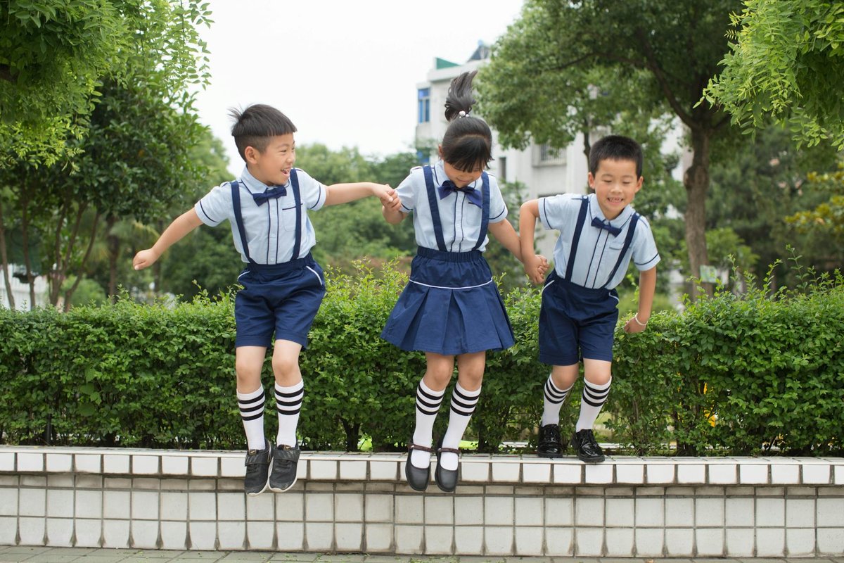 Three cheerful children in matching uniforms jump outdoors, enjoying a playful moment.