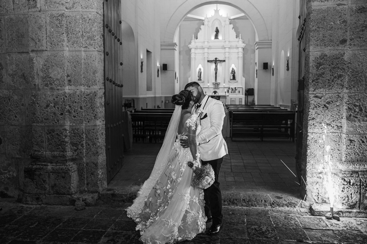 Bride and groom share a romantic kiss in a classic church setting.