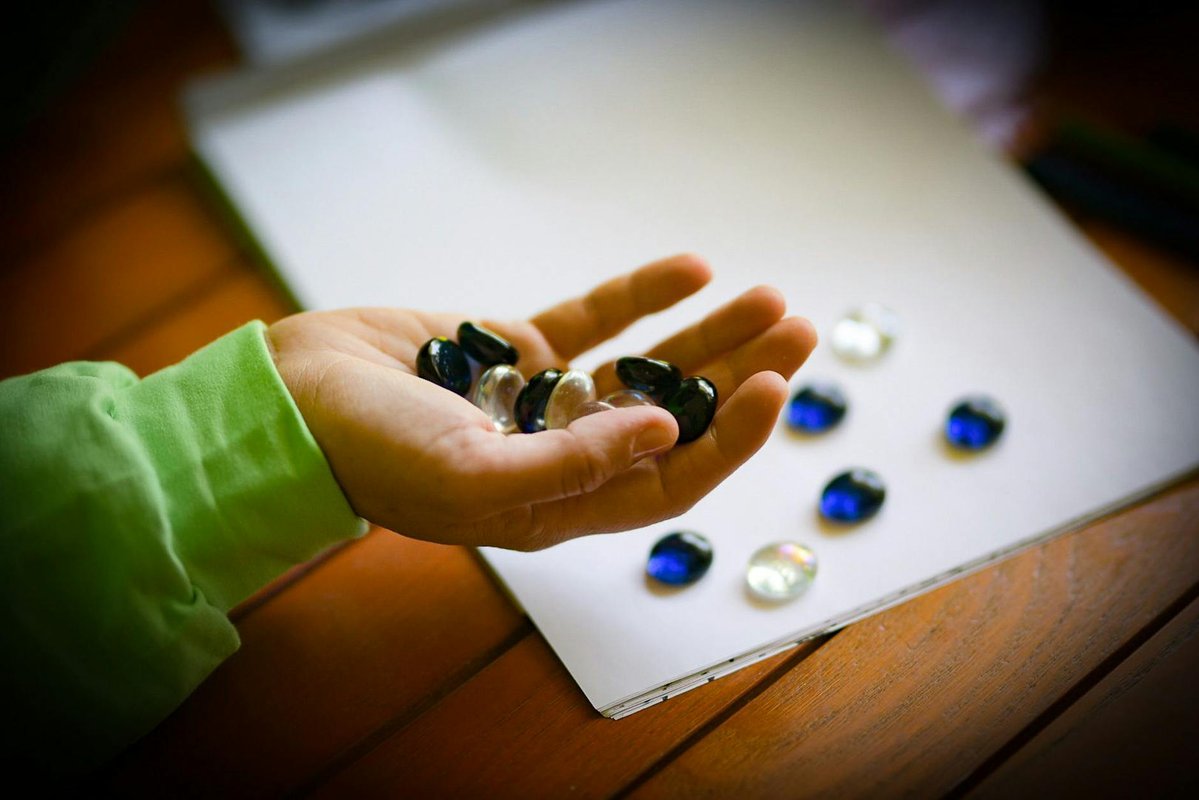 A hand holding black and white marbles over a wooden table with more marbles