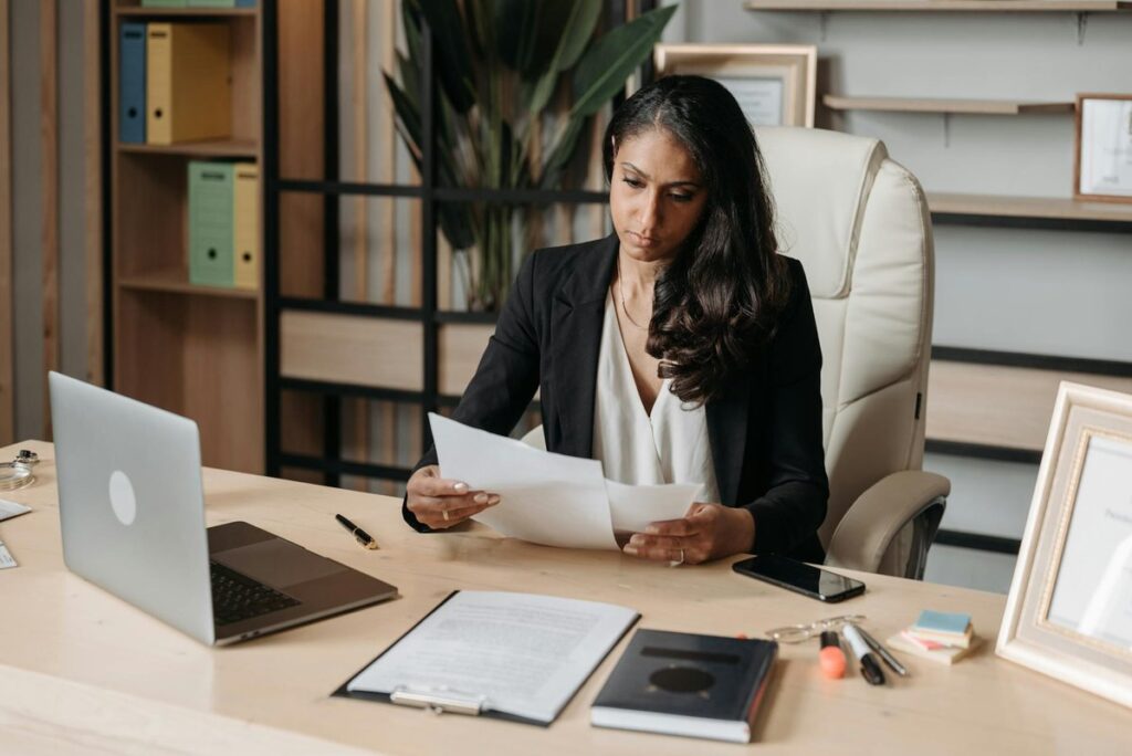 Business woman focused on paperwork at office desk, reviewing documents.