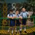 Three children in school uniforms standing on a playground bridge, posing confidently.