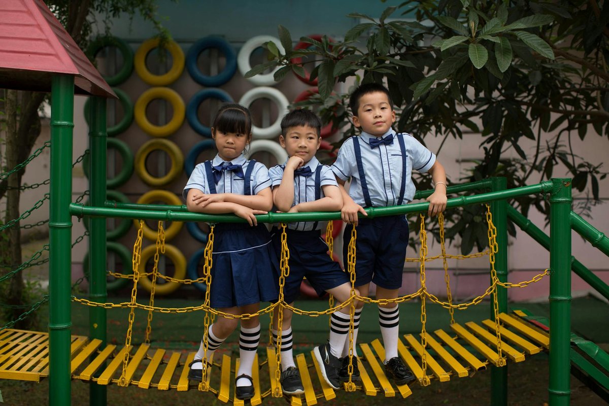 Three children in school uniforms standing on a playground bridge, posing confidently.