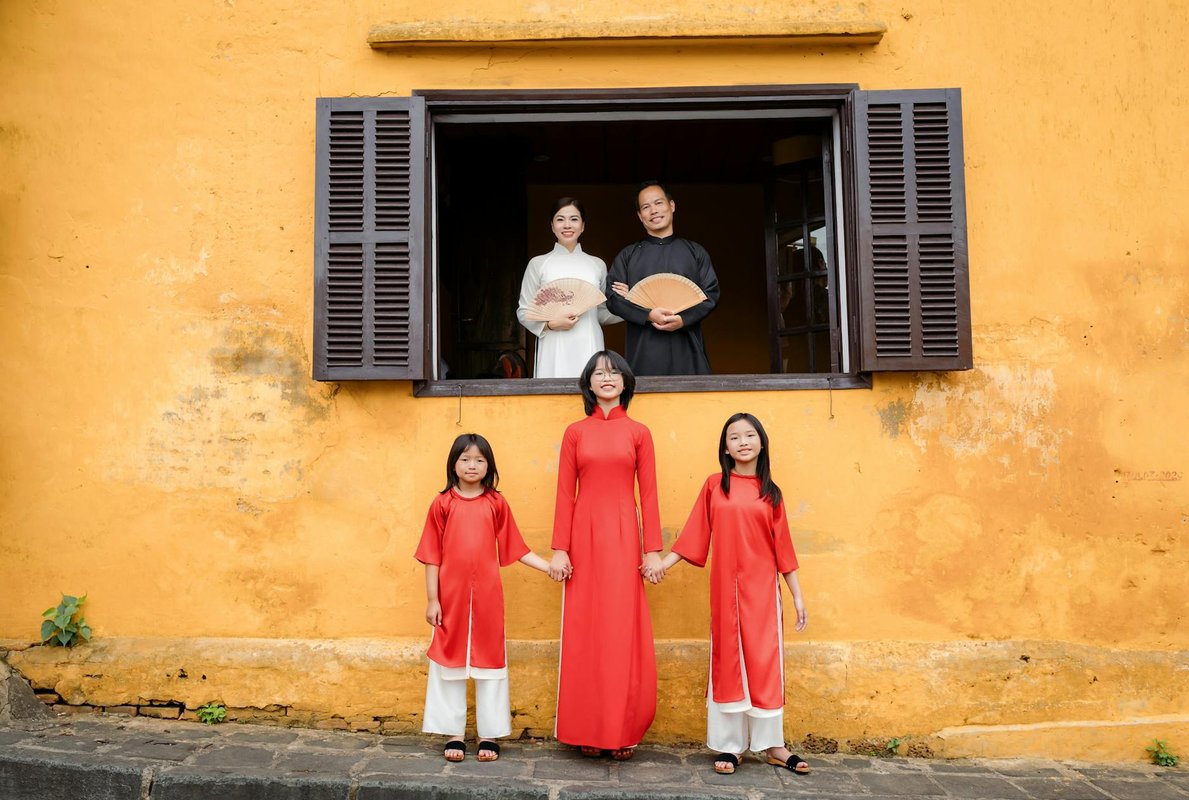 A family in traditional Vietnamese costumes posing against a yellow wall in Hội An.