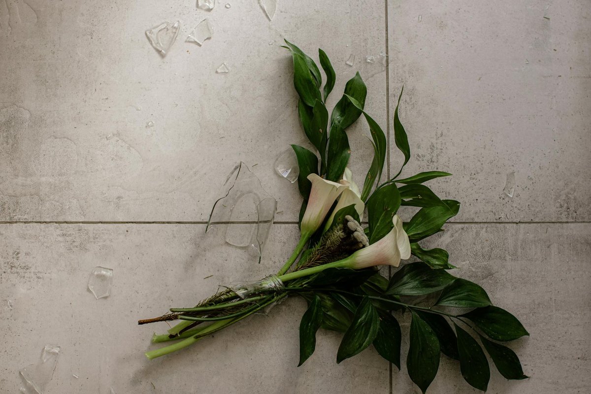 Beautiful calla lilies on a floor with broken vase shards around them.
