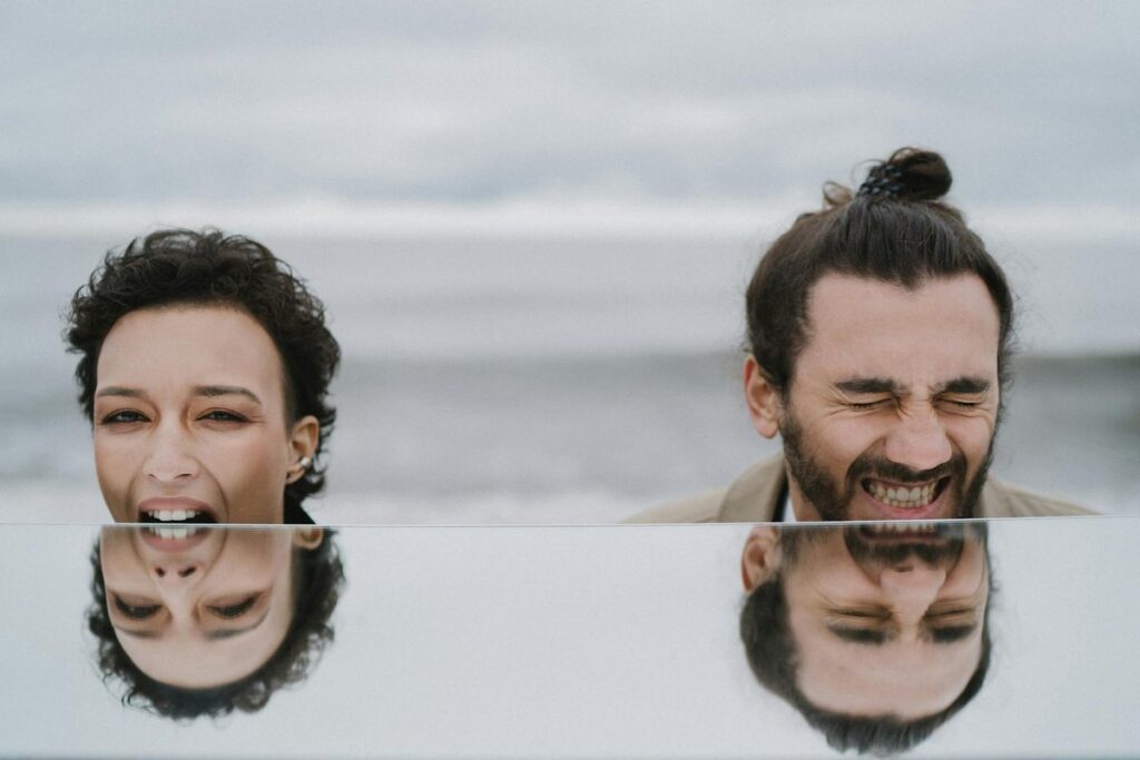A joyful couple shares a laugh at the beach, captured with their reflection.