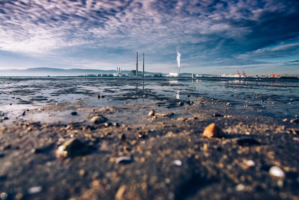 View of Dublin Bay with chimneys and industrial plant, reflecting on calm waters under a cloudy sky.
