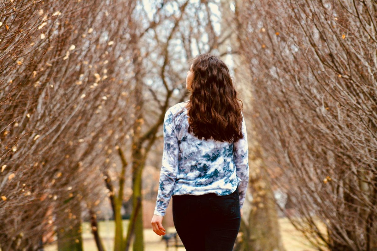 A woman in casual wear walks through a leafless park pathway, capturing the essence of fall.